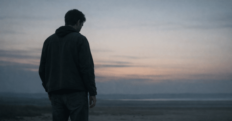 A person standing alone at dusk — tired of being patient, carrying a weight the world never sees.