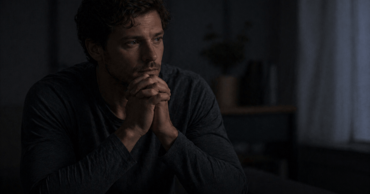 why does faith sometimes feel mechanical even when you still believe – a person sitting alone with hands clasped in prayer, looking distant and emotionally disconnected in a dark room